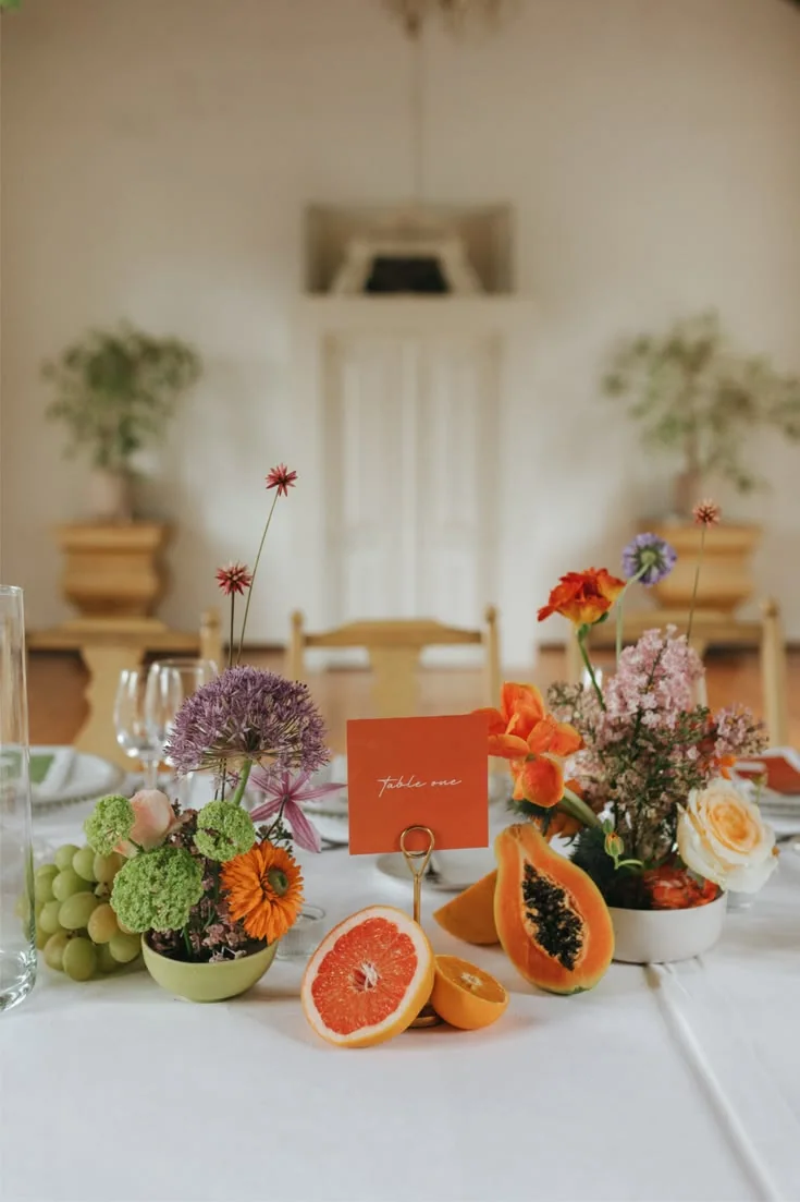 A wedding table set with glassware, colourful flowers, grapes and citrus fruit