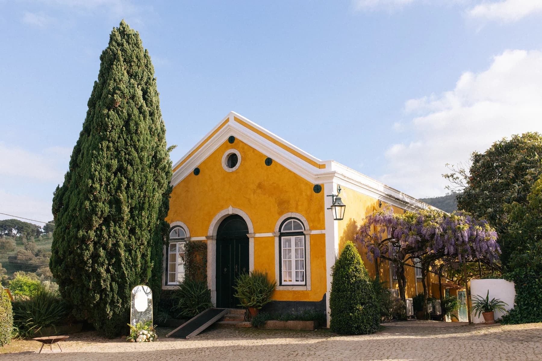 The yellow Dining Hall exterior beside a tall cypress and flowering wisteria