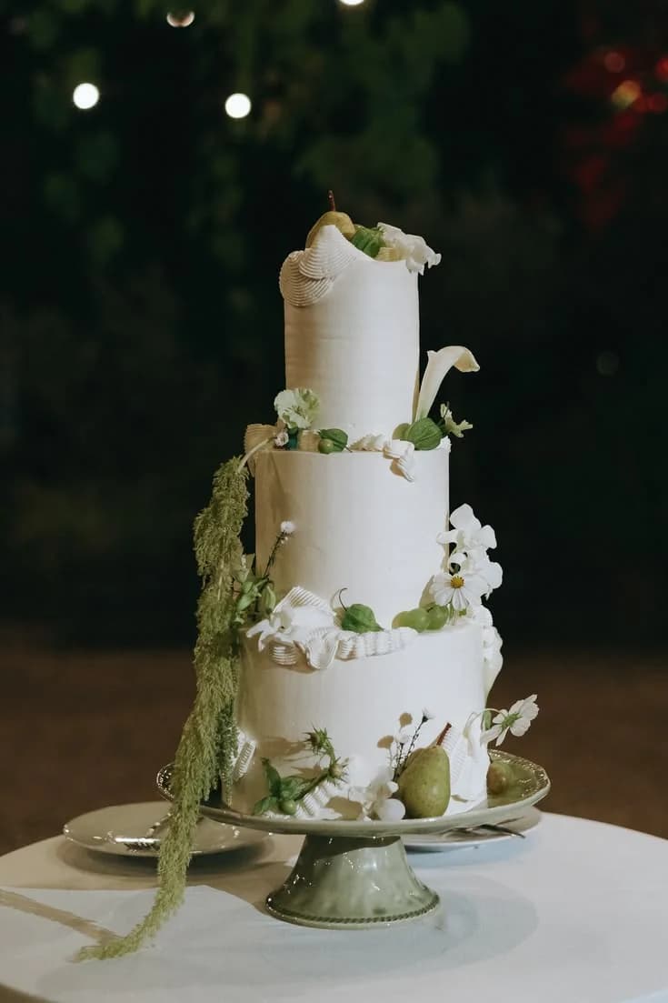A tiered white wedding cake decorated with greenery