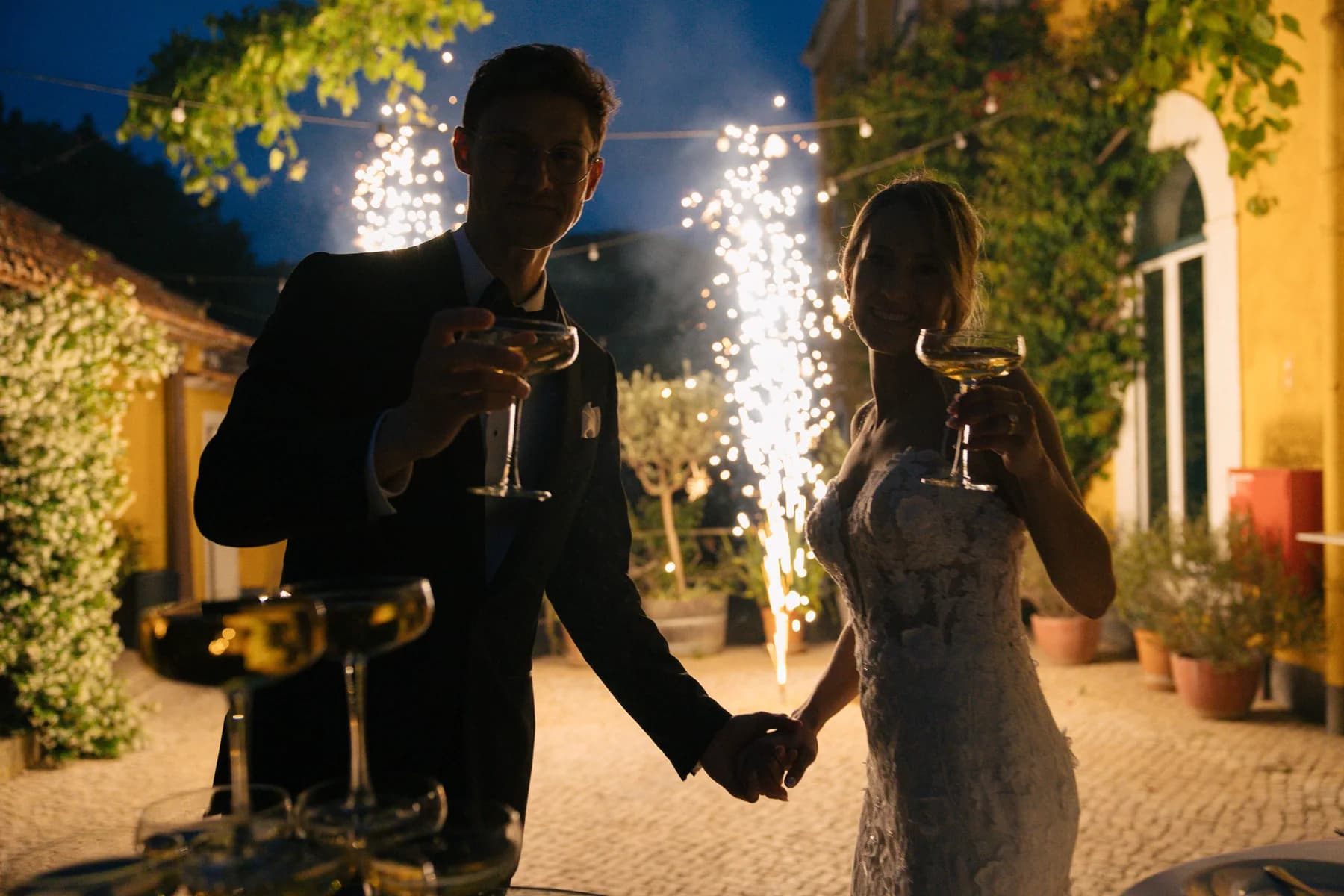 Newlyweds raising their glasses beside courtyard sparklers