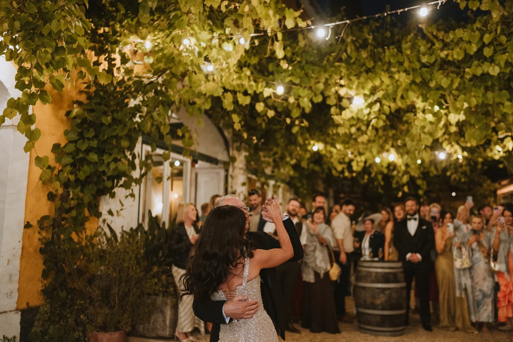 A couple dancing beneath courtyard vines and string lights