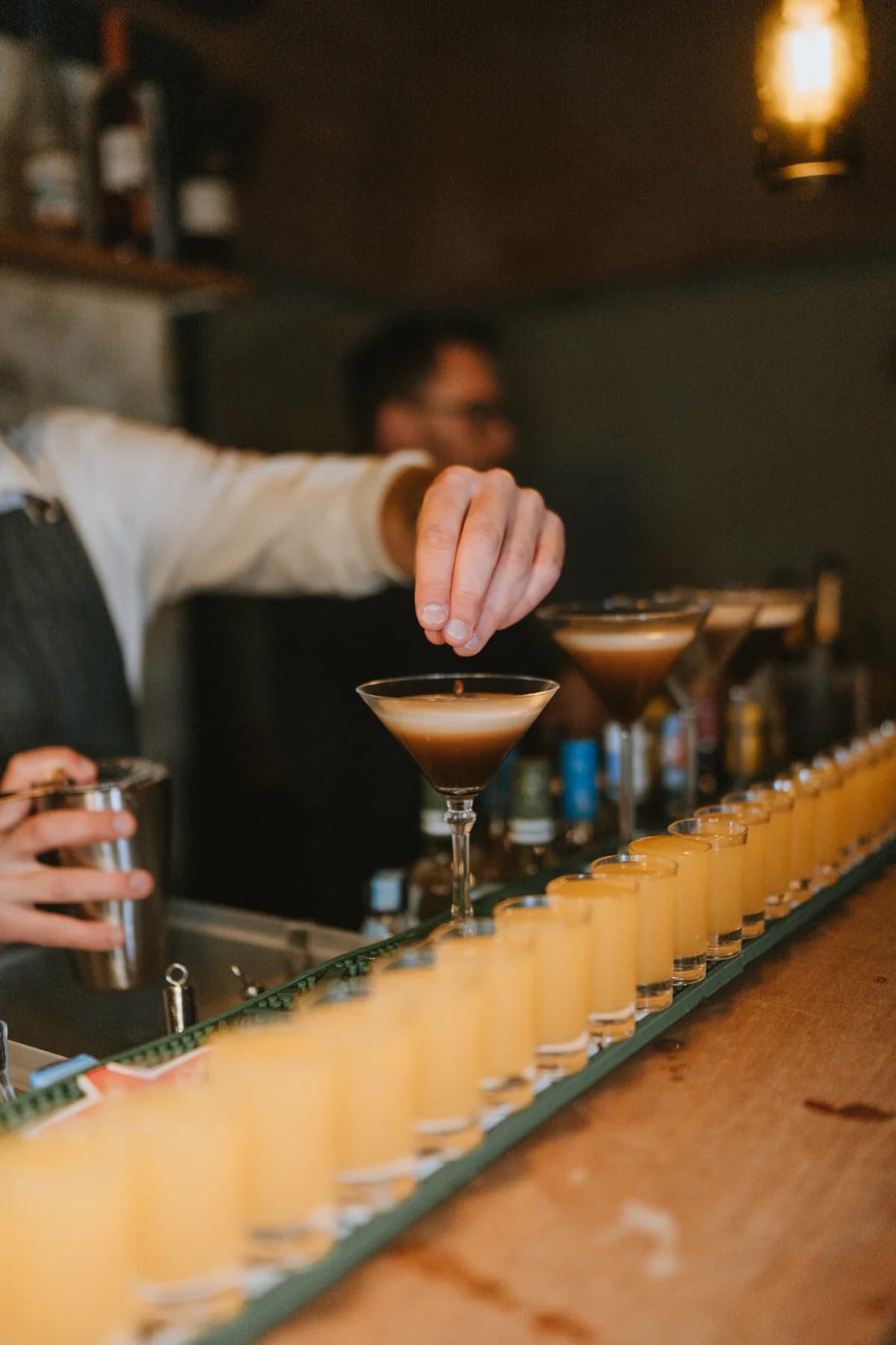 A bartender pouring a row of cocktails
