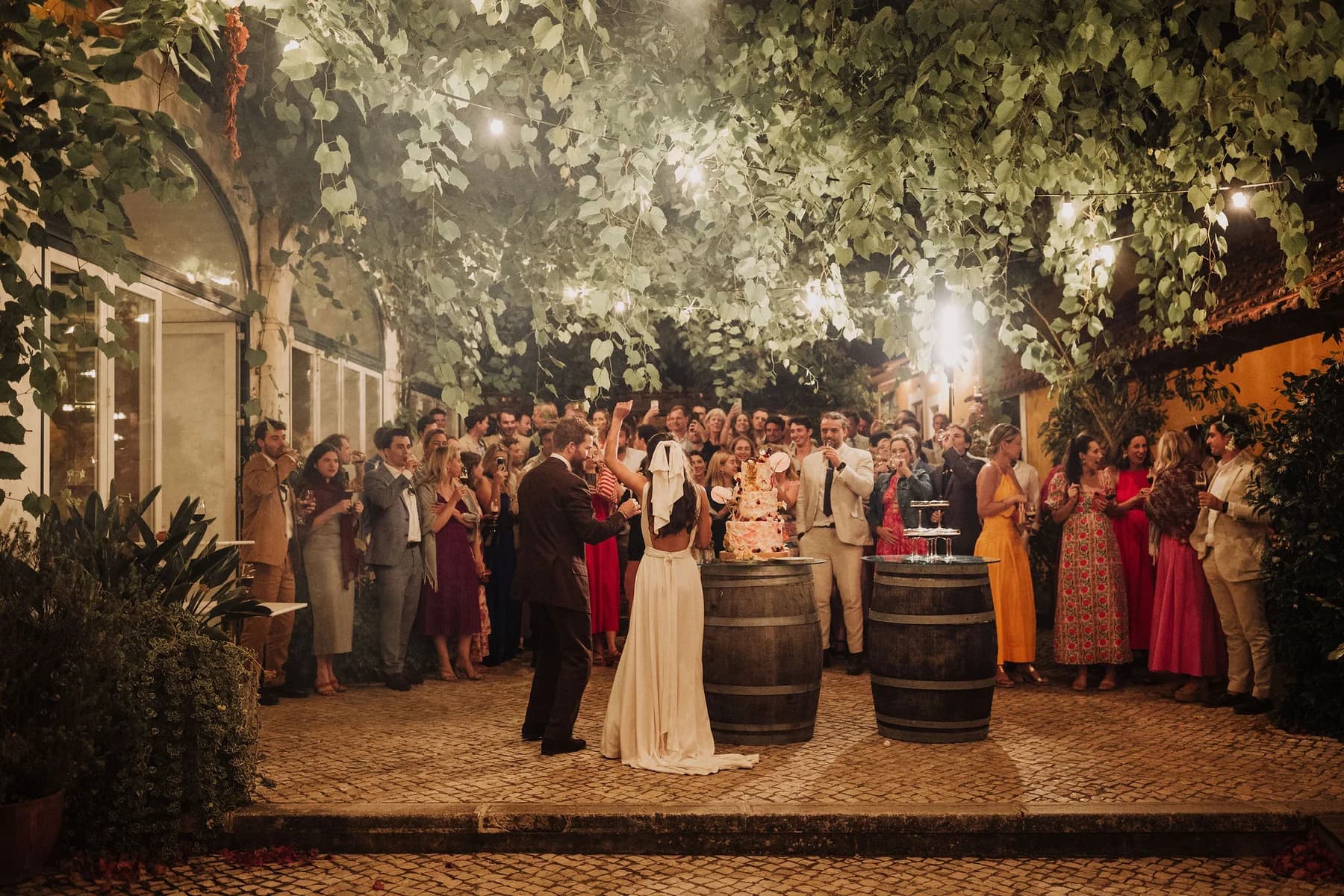 A couple celebrating with guests beneath illuminated courtyard vines