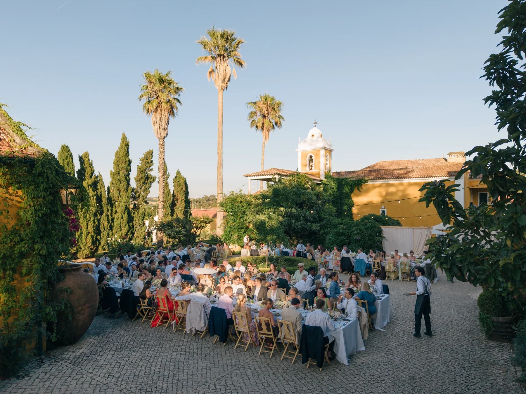 Guests dining outdoors beneath palm trees and the chapel tower