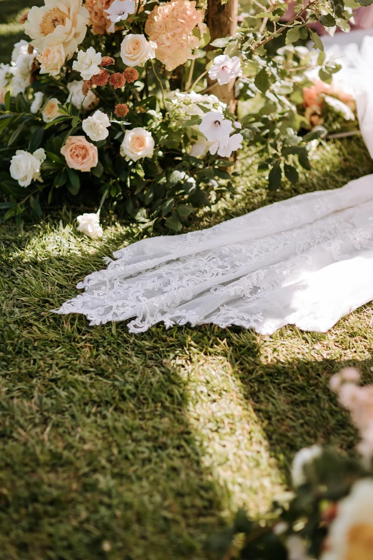 A bride's lace train beside pastel ceremony flowers