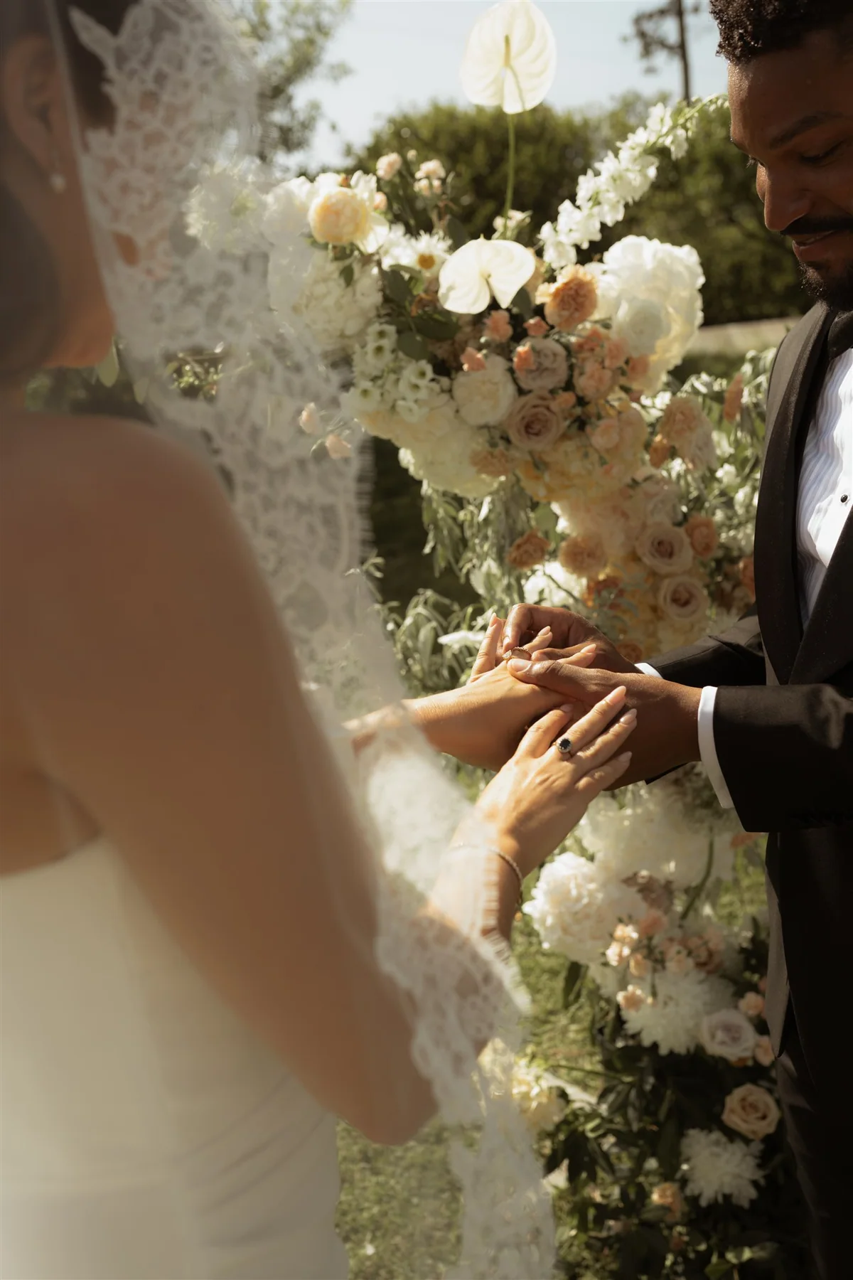 A couple exchanging rings beside white ceremony flowers