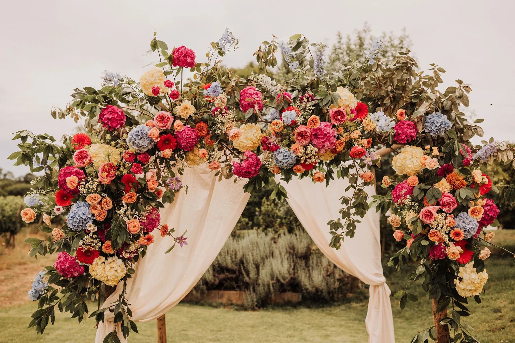 A colourful floral ceremony arch with cream drapery