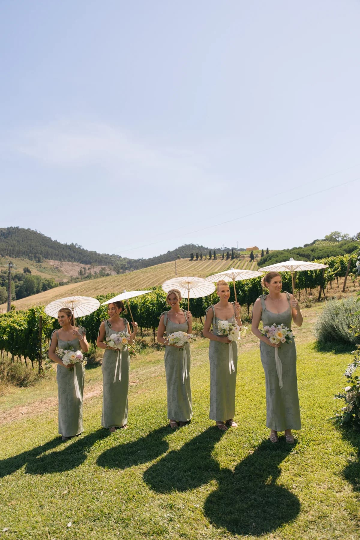 Bridesmaids holding white parasols on the ceremony lawn