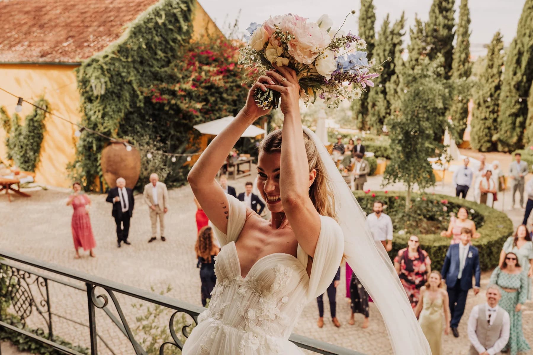 A bride holding her bouquet overhead on the courtyard steps