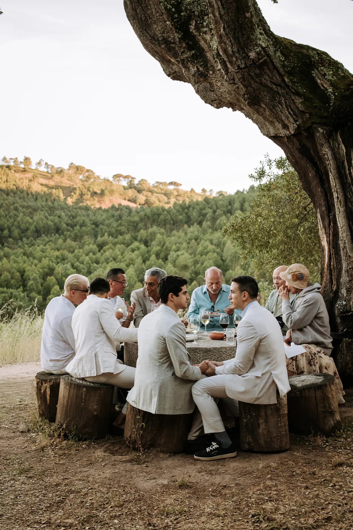 Guests sharing drinks around a table beneath a large tree