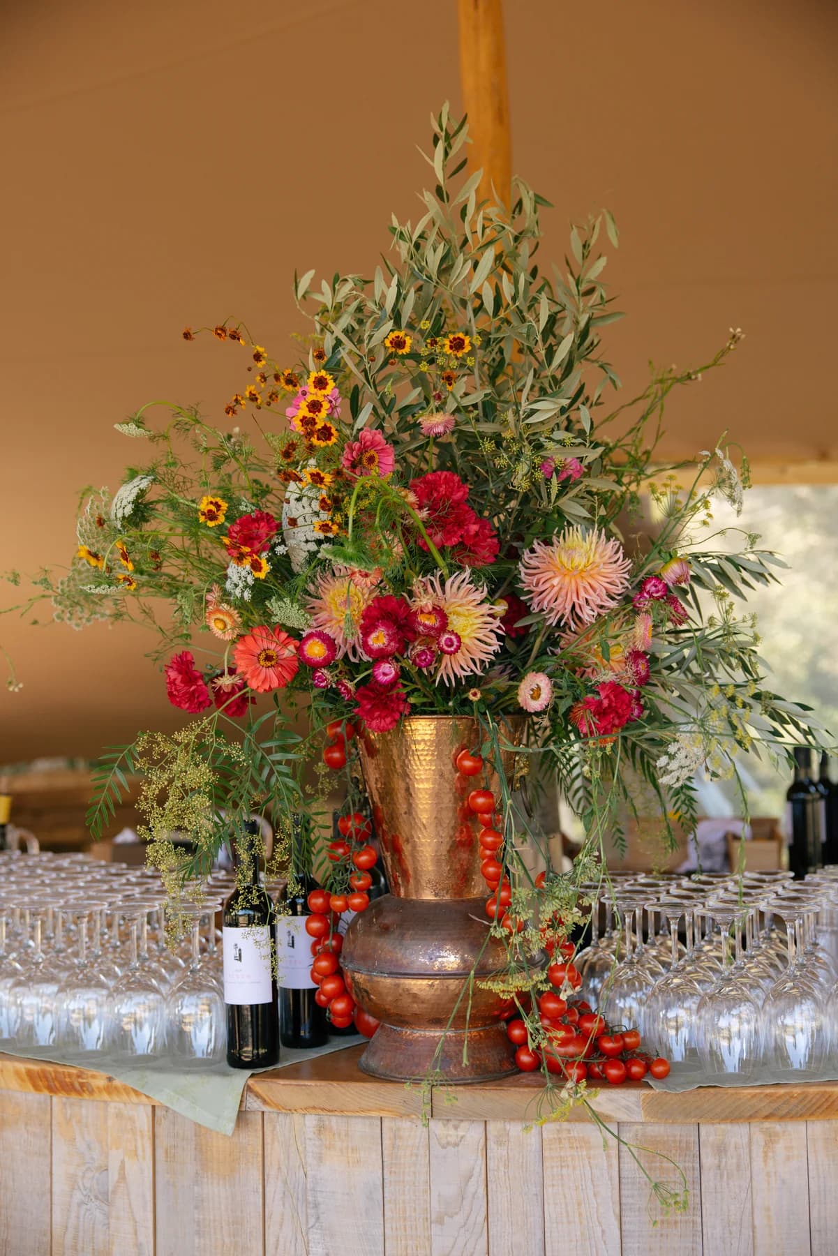 A colourful floral arrangement beside bottles and glasses