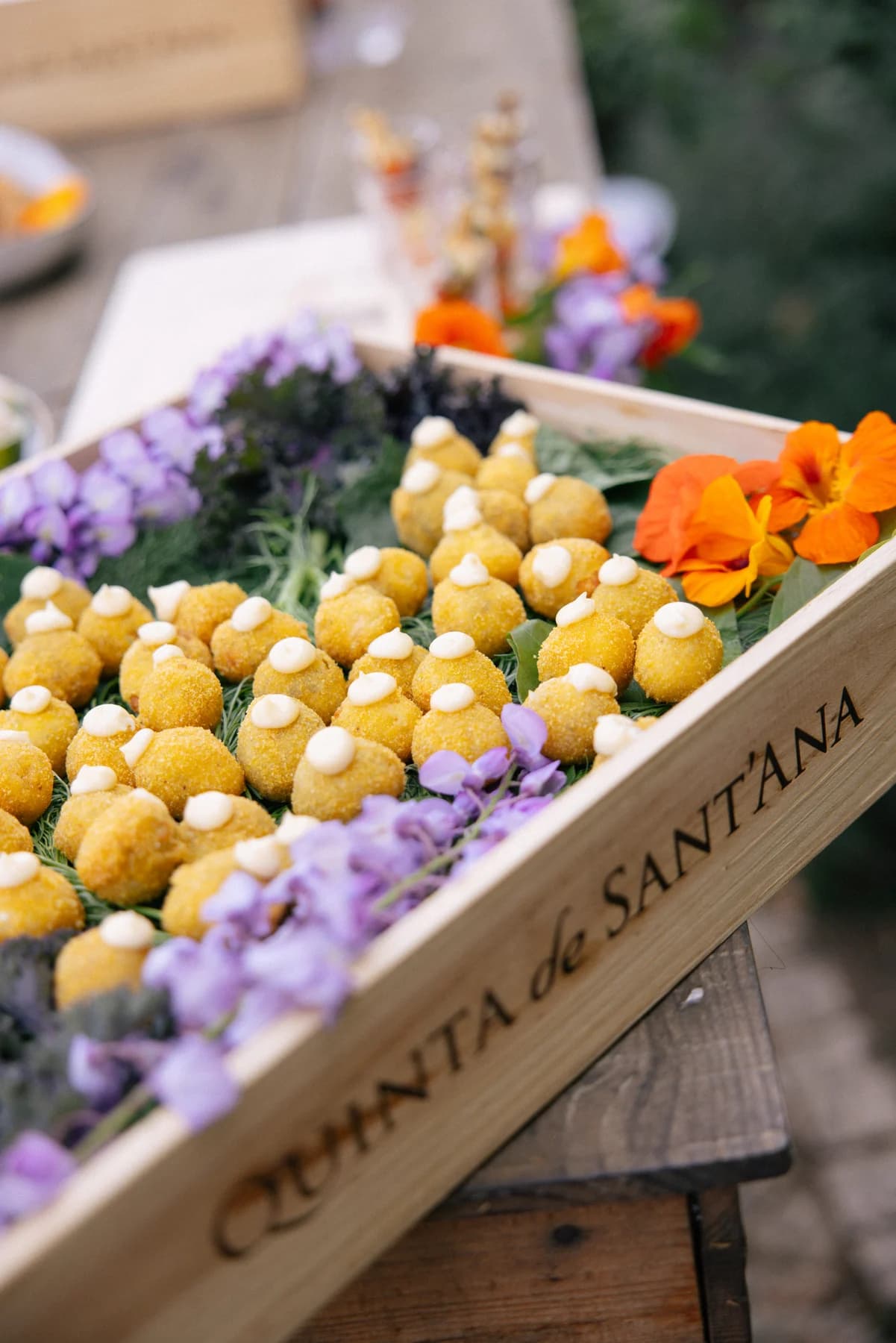 Golden canapés arranged with colourful flowers in a wooden Quinta de Sant’Ana tray