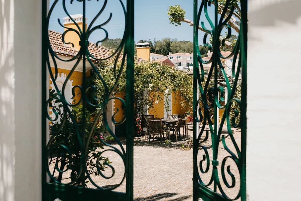 Open green wrought-iron gates framing a sunlit courtyard at the Quinta