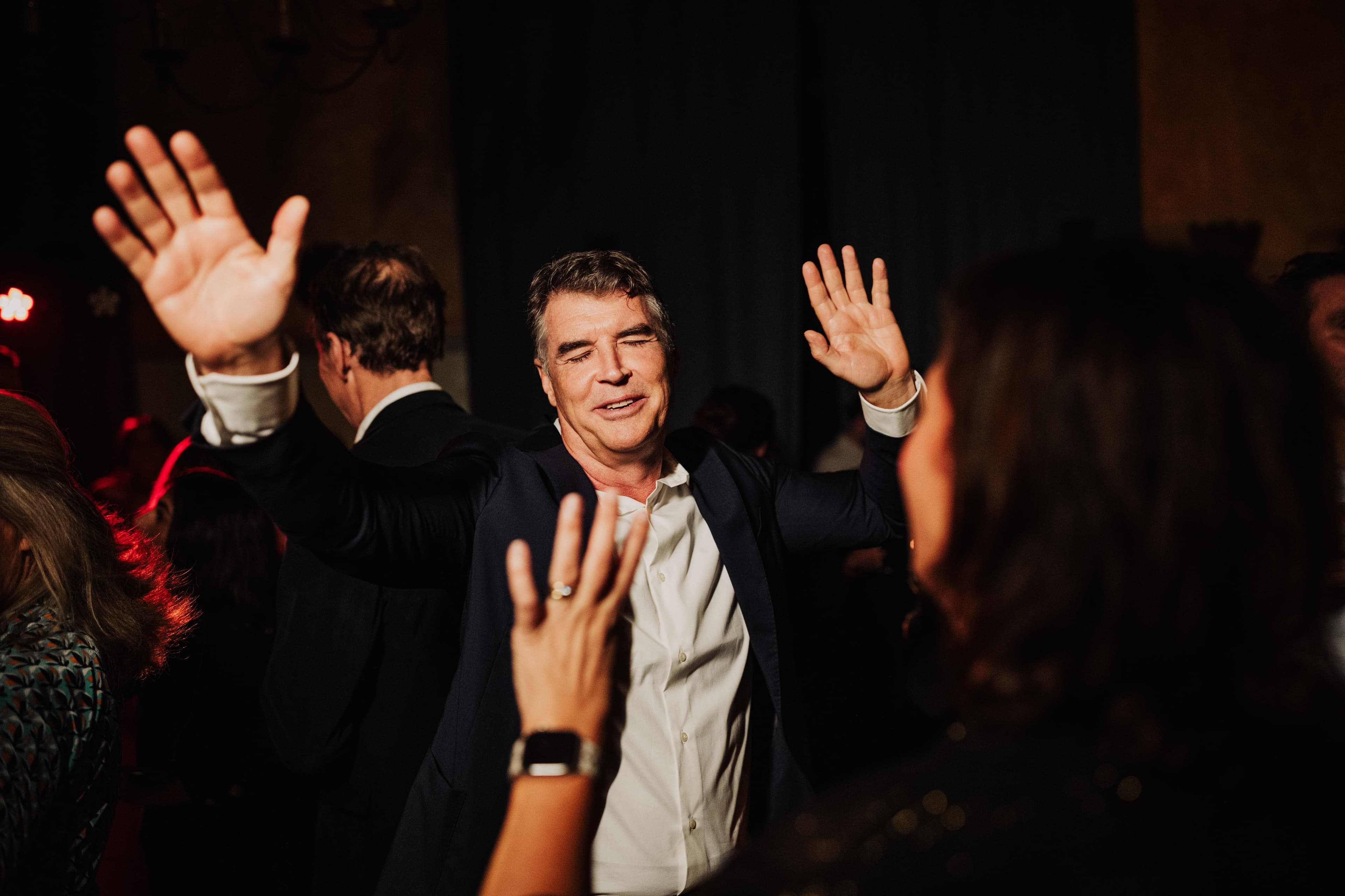 A wedding guest with his hands raised on the indoor dance floor