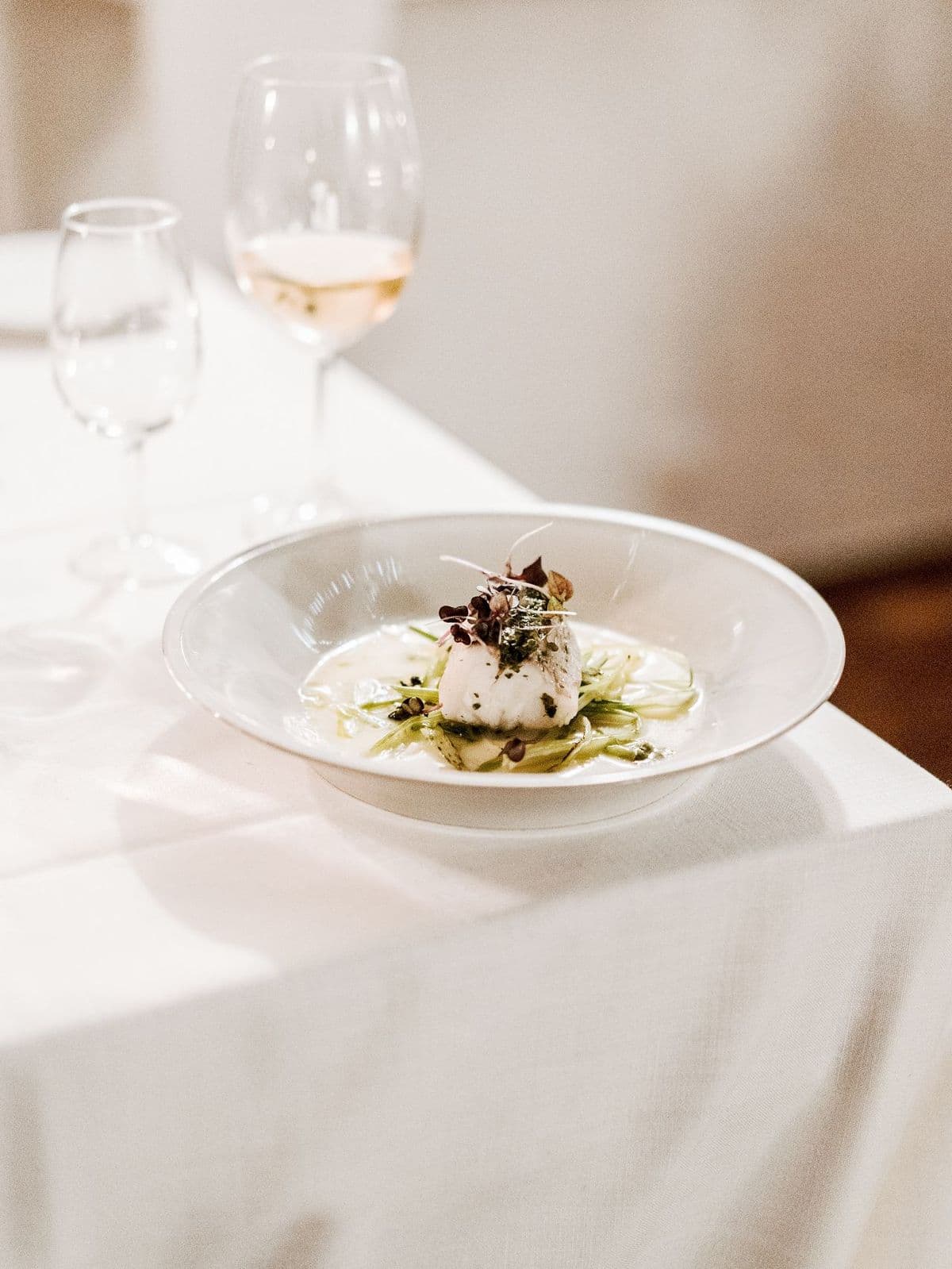 A plated fish course served with vegetables at a linen-covered dinner table