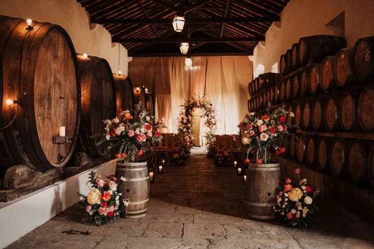 Flowers and candles lining an indoor ceremony aisle between the Adega's wine barrels