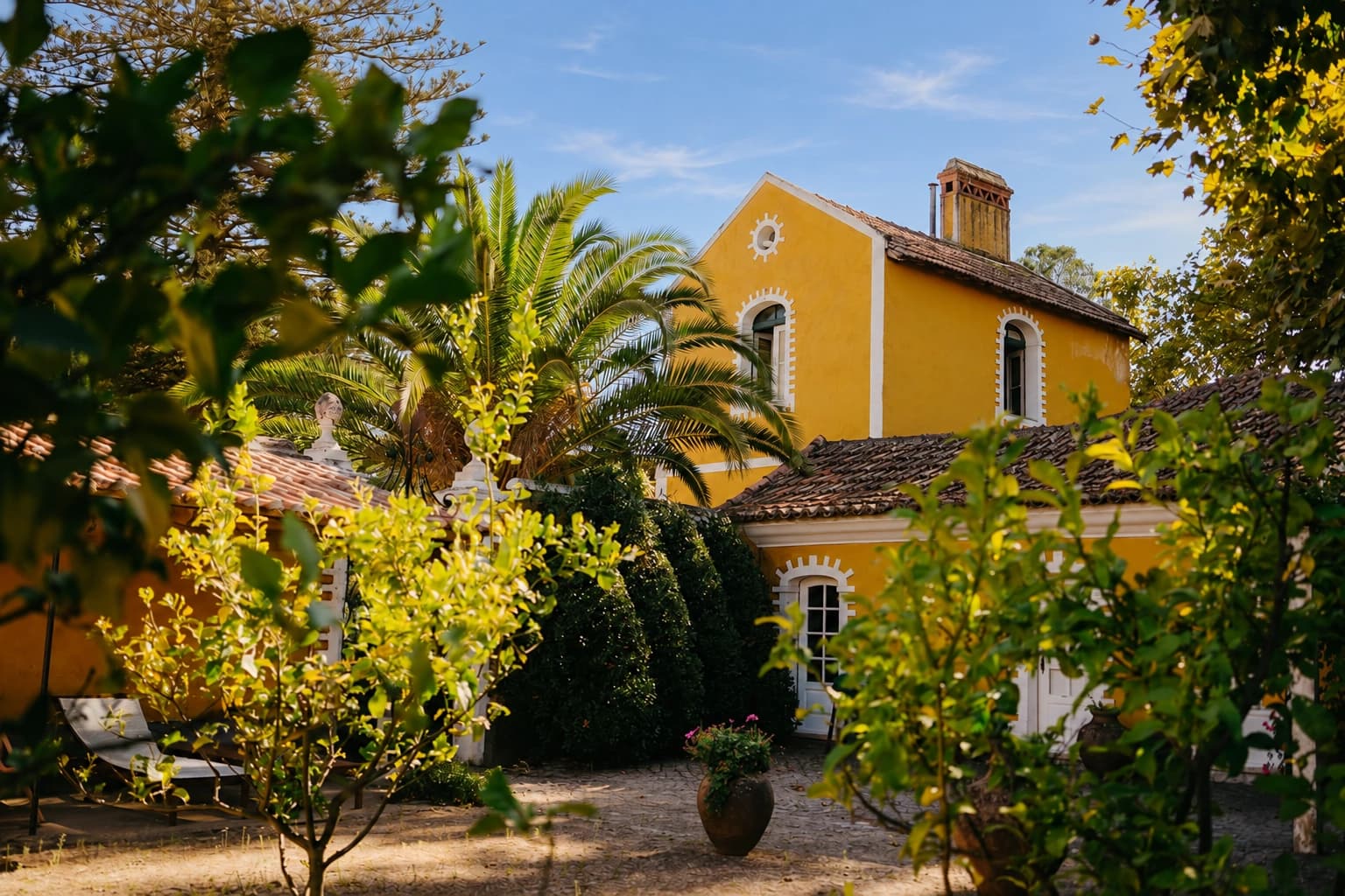 Yellow facade of Lemon Garden House framed by trees and flowering plants