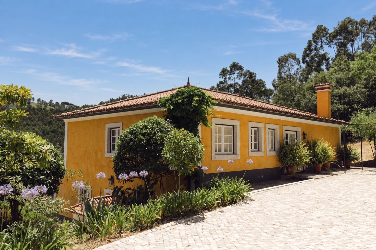Marreco House's yellow facade and flower beds beside the gravel drive