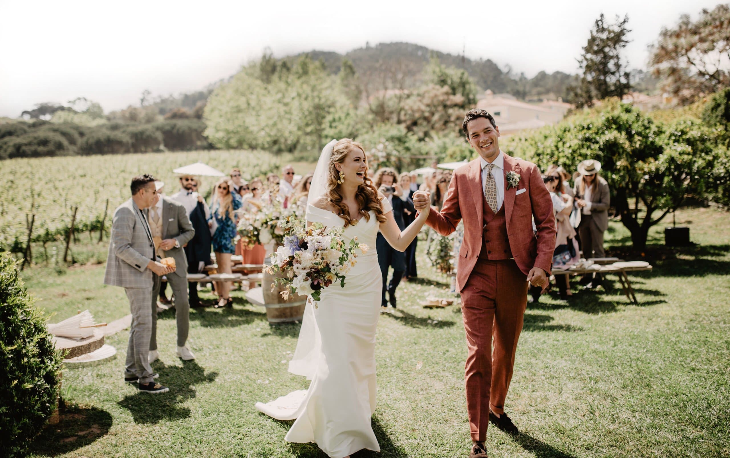 Newlyweds walking back up the vineyard ceremony aisle as guests applaud
