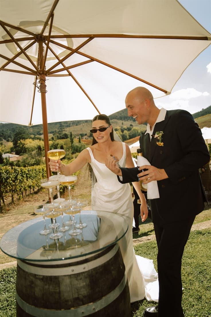 Couple with champagne on a wine barrel, vineyard behind