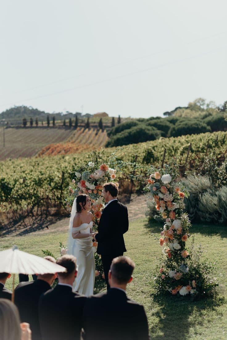 Ceremony under a floral arch with vineyard backdrop