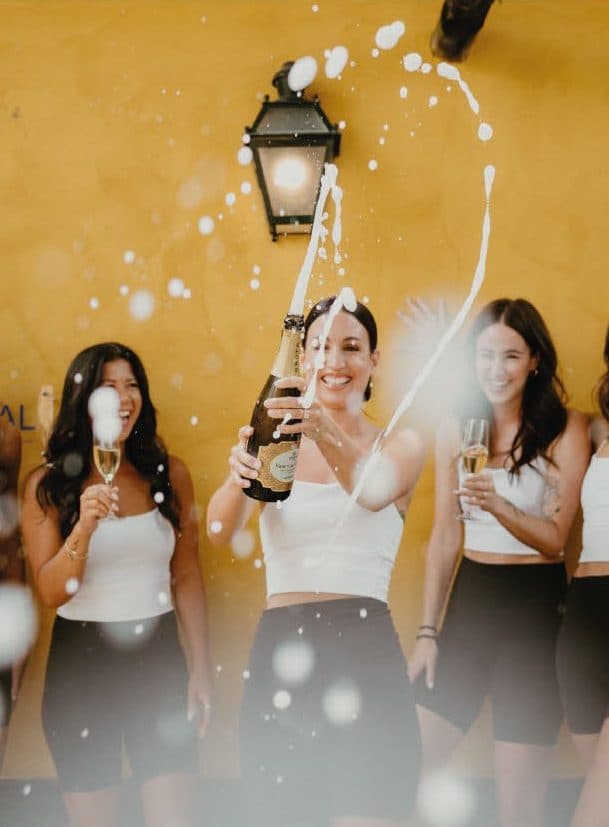 Friends laughing together as they open a bottle of sparkling wine at the Quinta